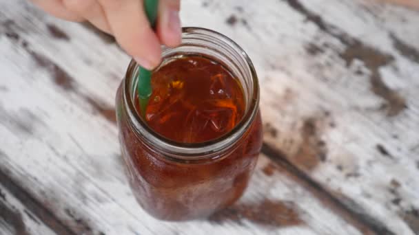 Bovenaanzicht van vrouwelijke handen die een ijsthee roeren in een pot met een plastic rietje. Houten tafel op achtergrond — Stockvideo