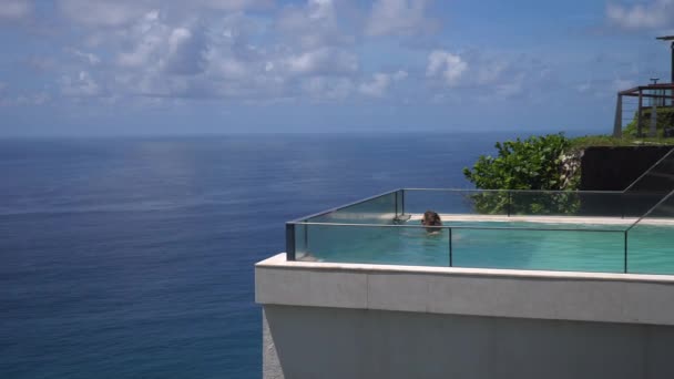 Ampla foto de uma mulher nadando na piscina de borda infinita com vista para um oceano — Vídeo de Stock