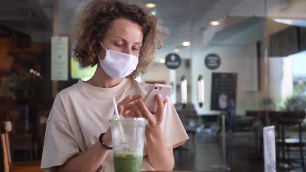 Caucasian girl texting in a coffee place. Coffee break with a smartphone and matcha latte — Stock Video