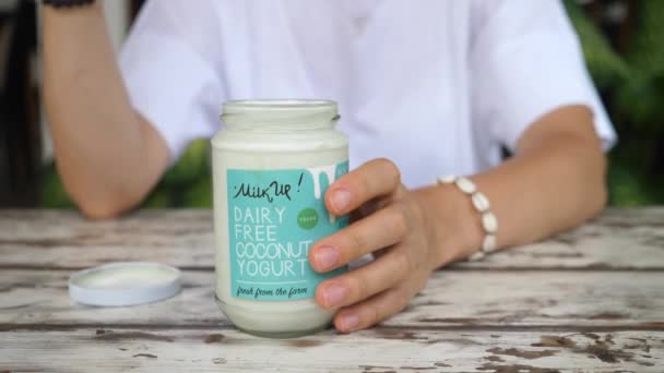 Las manos femeninas toman una cucharada de jogurt de coco del frasco y se lo muestran a la cámara. Promover productos libres de crueldad saludables — Vídeos de Stock