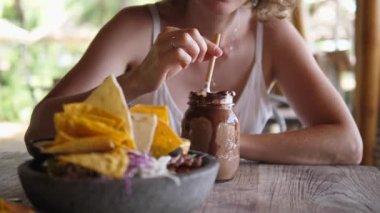 Güzel sarışın kadın, plaj restoranında tek başına öğle yemeği yerken çikolatalı milkshake 'inin tadını çıkarıyor. Tek başına seyahat