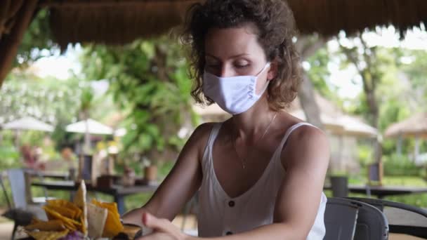 Almuerzo de estilo mexicano en un café de playa. Caucásico chica en un mascarilla tira más cerca bowl con nachos y mira con alegría — Vídeos de Stock