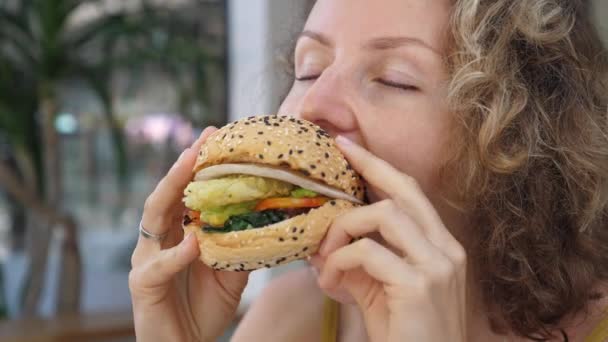 Närbild av hungriga kaukasiska kvinna som tar bett av läckra veganska hamburgare med stor aptit — Stockvideo