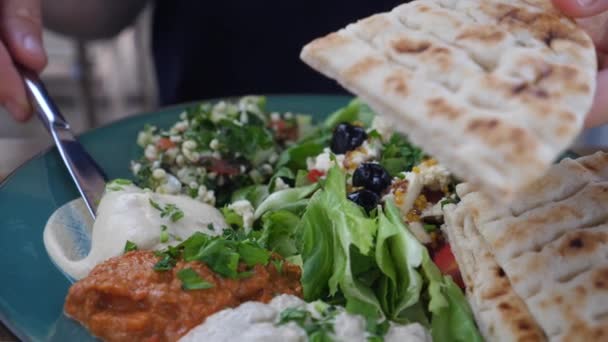 Hand spreading hummus on pita. Meze plates with salad, dips and pita. Healthy organic middle eastern cuisine. — Stock Video