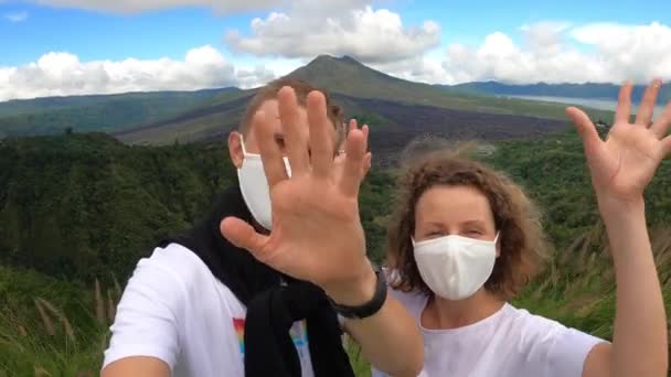 Joven pareja caucásica en máscaras faciales hablando en videollamada con las montañas y el océano en el fondo. Escapada romántica durante la pandemia de covid-19 — Vídeos de Stock