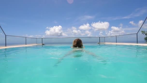 Camera na vrouwelijk zwemmen in een infinity zwembad met uitzicht op een oceaan — Stockvideo