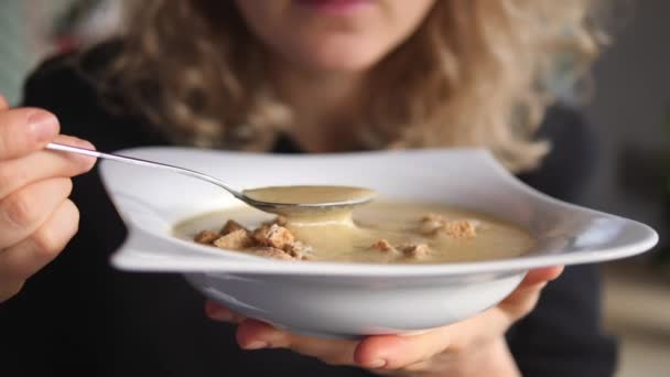 Mulher jovem com cabelo encaracolado loiro comendo sopa de creme de cogumelos com croutons. — Vídeo de Stock