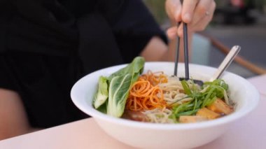 Öğle yemeğinde Ramen çorbası. Beyaz kasedeki eriştenin tadını çıkaran aç genç bir kadın. 