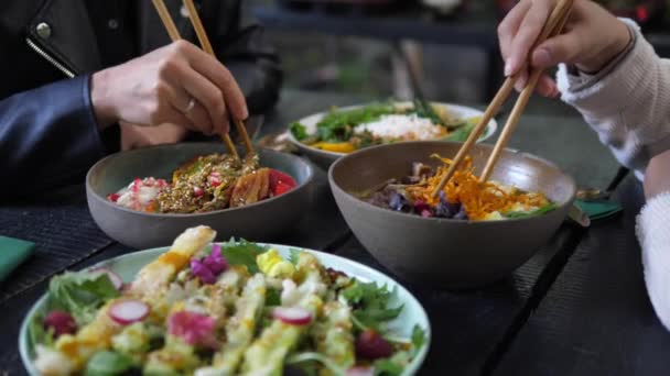 Egészséges ázsiai vegán ebéd a rusztikus kávézóban. Két ember evőpálcikával eszi az egészséges vegán ételét. — Stock videók