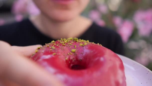 Primo piano della bocca femminile affamata che morde ciambella glassata rosa vegana e rimette su un piatto rosa pastello — Video Stock