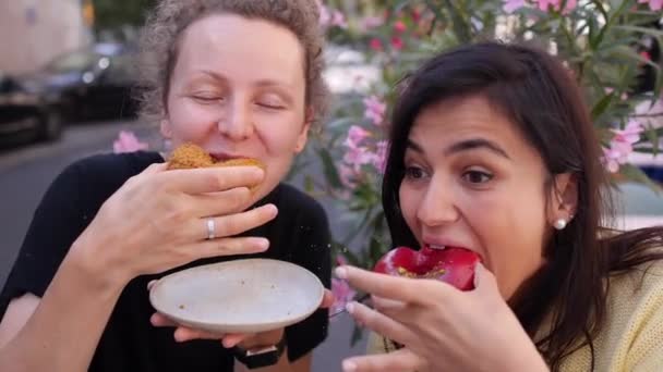Portret van twee vrolijke meisjes die plezier hebben met het proberen van verschillende donuts. Een maaltijd delen met vrienden — Stockvideo