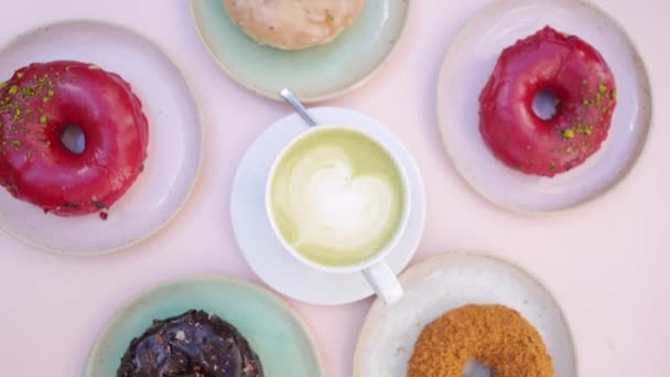 Draufsicht auf das sich drehende Bild von Matcha Latte, umgeben von bunten Donuts. — Stockvideo