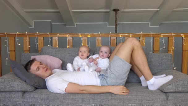 Pai cansado dormindo no sofá com seus bebês gêmeos em casa. Conceito de bebê e pai. — Vídeo de Stock