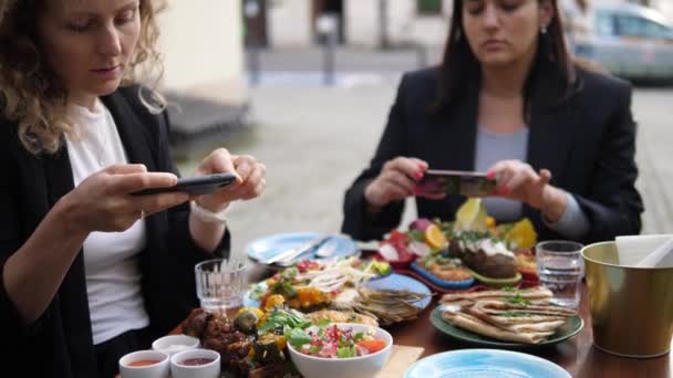 Två unga kvinnor tar bilder av sin hälsosamma vegan lunch. En livsmedelsbloggares arbete — Stockvideo