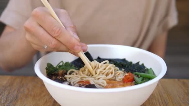 Female pulling noodles out of vegan ramen soup with chopsticks and showing it to the camera. Healthy balanced vegan diet — Stock Video