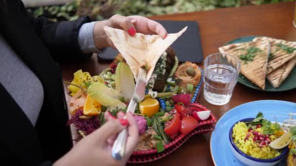 Женские руки, распространяющие соусы на питу. Удивительная красочная мезе тарелка с разнообразными веганскими закусками ближневосточного стиля — стоковое видео