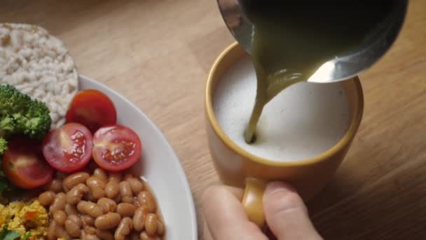 Blick von oben auf das Eingießen von Matcha-Tee in geschäumte pflanzliche Milch. Gesundes veganes Frühstück — Stockvideo