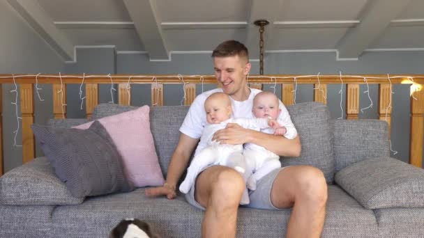 Junger Vater hält Baby-Zwillinge zu Hause mit Hund. — Stockvideo