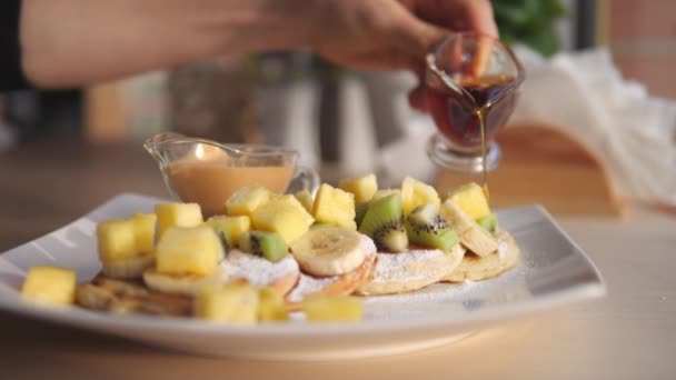 Mão derramando xarope de bordo ou agave em panquecas vegan com frutas para o café da manhã. — Vídeo de Stock