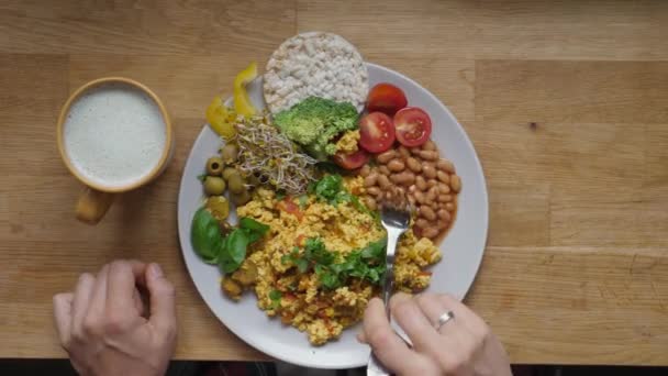 Draufsicht auf Frau, die veganes Frühstück mit Tofu-Omelett, Bohnen und Salat isst und pflanzliches Milchgetränk trinkt. Frühstück auf Holztisch serviert — Stockvideo