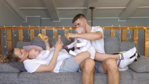 Família feliz com bebês gêmeos relaxando no sofá em casa. — Vídeo de Stock
