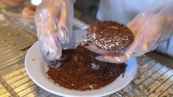 Handen in een wegwerphandschoenen bestrooi vers gebakken donut met chocolade — Stockvideo