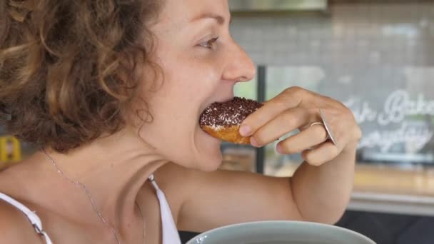 Inyección lateral de mujer caucásica tomando un bocado de donut fresco con gran apetito y lamiéndose los dedos — Vídeos de Stock