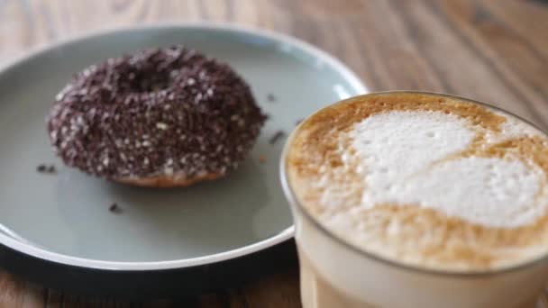 Cappuccino na bazie roślin podawane w szklance z pączkiem pokrytym posypką czekoladową — Wideo stockowe
