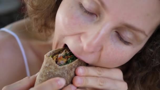 Close-up van een blank meisje eten gezonde heerlijke veganistische wrap met enorm plezier. . — Stockvideo