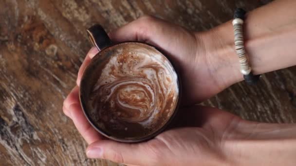 Top view of female hands holding a mug of hot chocolate on wooden background. Rotating shot — Stock Video