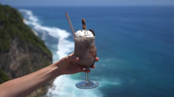 Milkshake vegano al cioccolato con panna montata decorato con biscotti Oreo tenuti a mano su un bellissimo sfondo oceanico — Video Stock