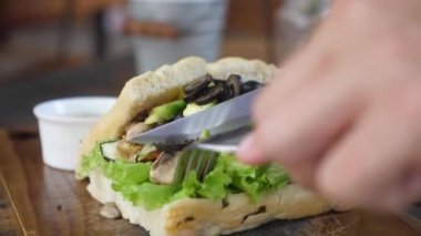 Eller sebze dolu, kablosuz çatal bıçak dolu bir sandviçi kesiyor.