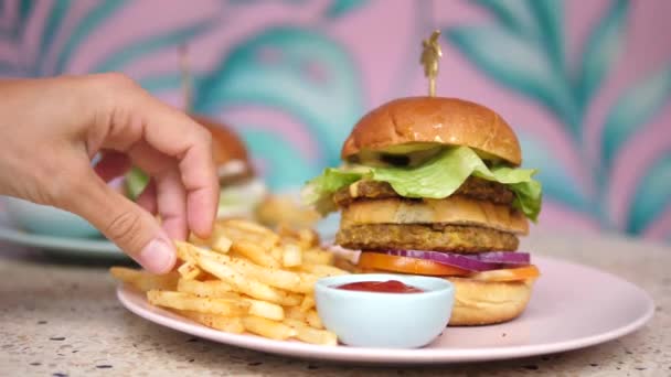 Vegan Street concept de nourriture. Une main prend une frite et l'enfonce dans du ketchup. Hamburger végétalien à deux étages sur l'assiette — Video