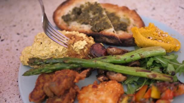 Primer plano de almuerzo vegano de tortilla de tofu, espárragos, hummus, tostadas y verduras a la parrilla. Tenedor mostrando tortilla a la cámara — Vídeos de Stock