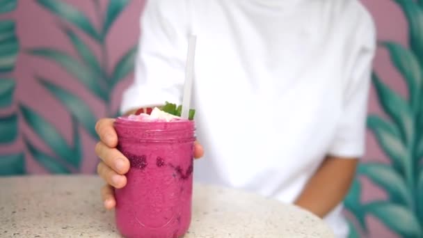 Femme blanche prenant une gorgée de smoothie aux baies dans un bocal en verre. Murs roses avec des feuilles peintes sur le dos — Video