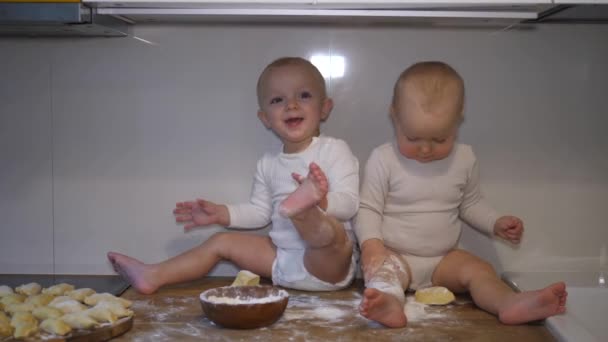 Mutfak masasında oturmuş hamur ve unla oynayan iki beyaz bebek.. — Stok video