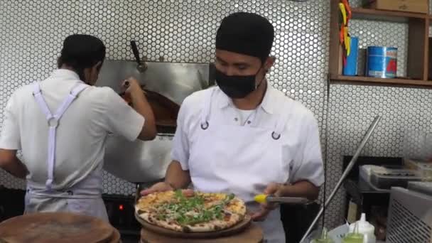พ่อครัวพิซซ่าเพิ่มชีสตะแกรงบนพิซซ่าอบสดและวางไว้บนถาดไม้ บาหลี-ธันวาคม-2020 — วีดีโอสต็อก