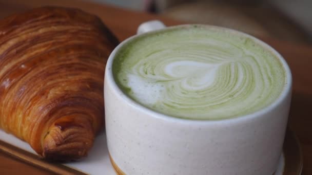 Mugg matcha te latte serveras med färska croissanter. Handen tar bort en mugg — Stockvideo