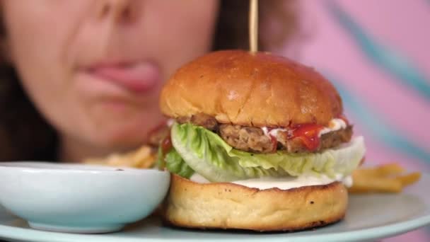 Tutup gadis lapar menjilat bibirnya di depan burger vegan — Stok Video