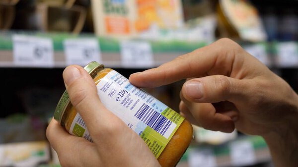 Женщина читает этикетки на банке детской еды. Сознательные покупки в бакалее.