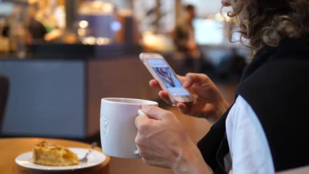 Close-up van de handen met behulp van smartphone in een koffiehuis en het houden van witte porseleinen mok — Stockvideo