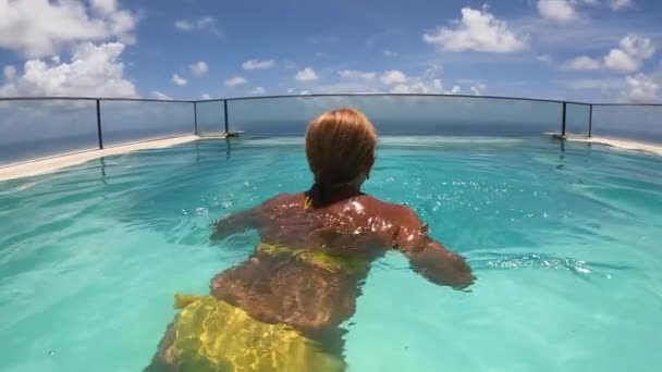 Задняя фотография женщины средних лет, плавающей в бесконечном бассейне с видом на океан — стоковое видео