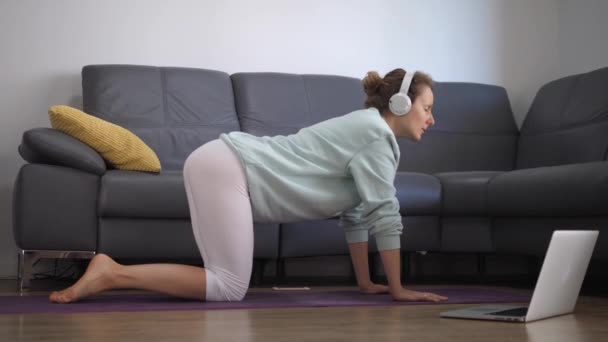 Joven mujer caucásica practicando yoga en línea en casa. Mantenerse en forma durante la pandemia de covid-19 — Vídeo de stock