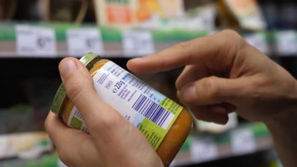 Mujer leyendo las etiquetas en un frasco de comida infantil. Compras de comestibles conscientes. — Vídeos de Stock