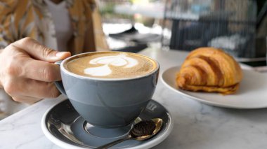 Bir kupa bitki esaslı latte servis eden kadın eller. Masada taze pişmiş kruvasan. 