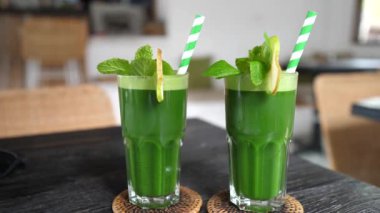 Two glasses of organic green smoothies decorated with mint leaves. Sustainable paper straw