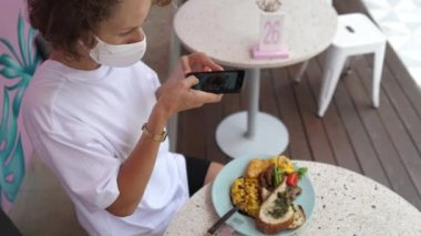 Kafkas kadın yemek blogcusunun akıllı telefonuyla vejetaryen kahvaltısının fotoğrafını çekmesi. Covid-19 salgını sırasında dışarıda yemek.