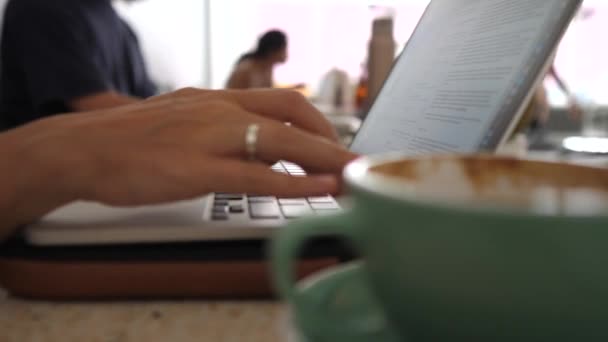 Concepto de trabajo remoto. Primer plano de las manos femeninas escribiendo en un ordenador portátil y beber café. — Vídeos de Stock