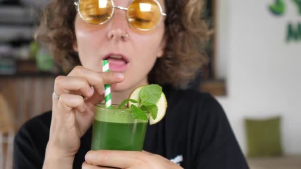 Vieroitus ja puhdistaa käsite. Iloinen tyttö oranssissa sävyissä juo vihreää orgaanista kylmäpuristettua mehua — kuvapankkivideo