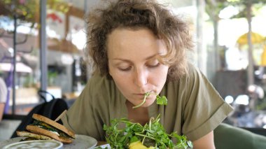 Aç, neşeli genç kadın elsiz vejetaryen tostunu yiyor.